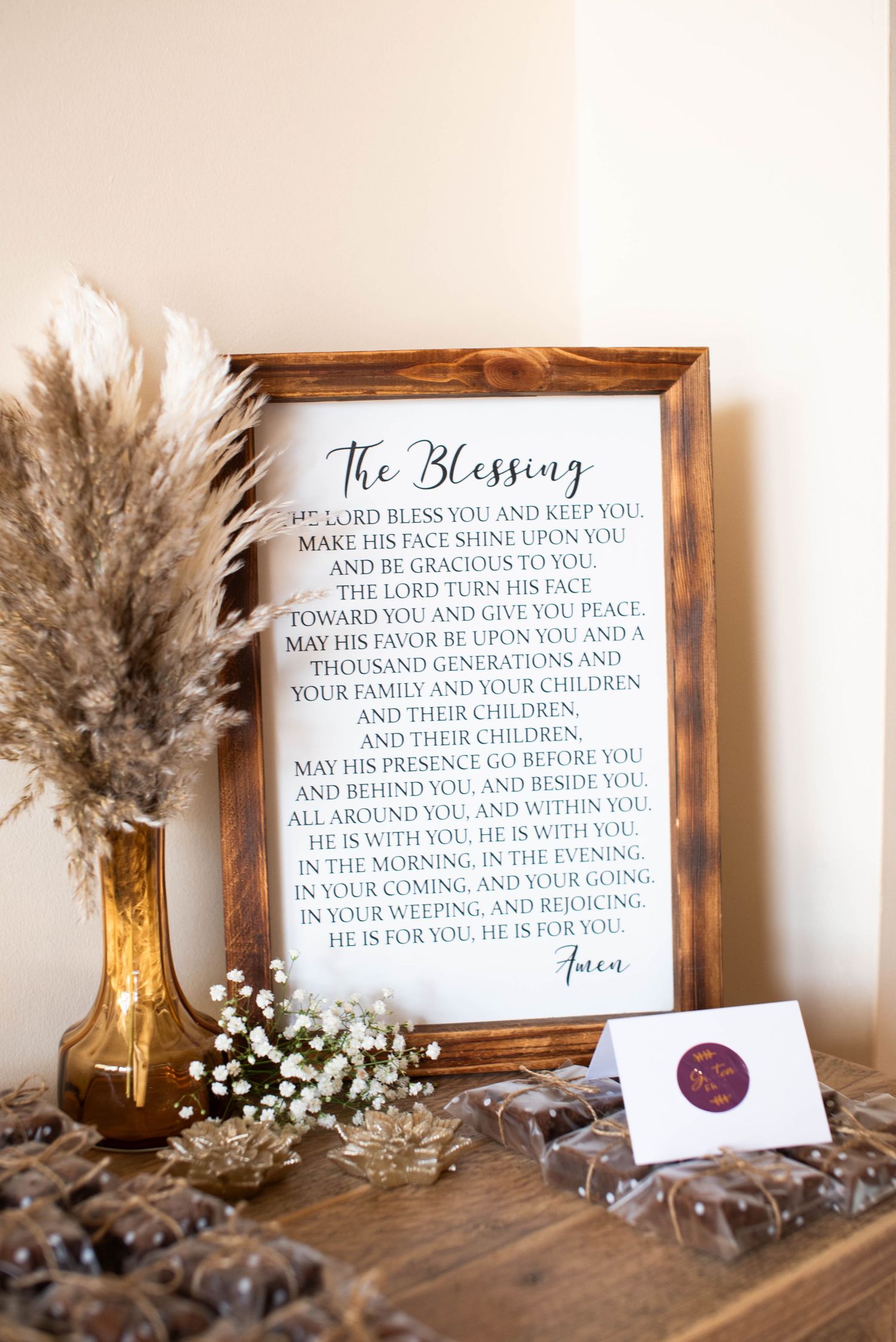 Framed wedding blessing sign surrounded by pampas grass, baby's breath, and chocolate favors.