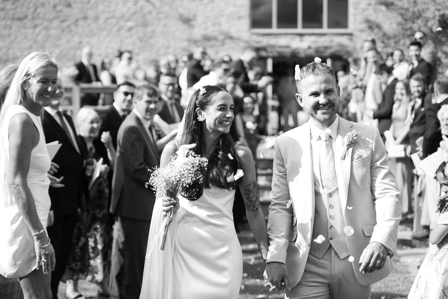 Newlyweds walk joyfully through confetti after their outdoor wedding ceremony surrounded by guests.