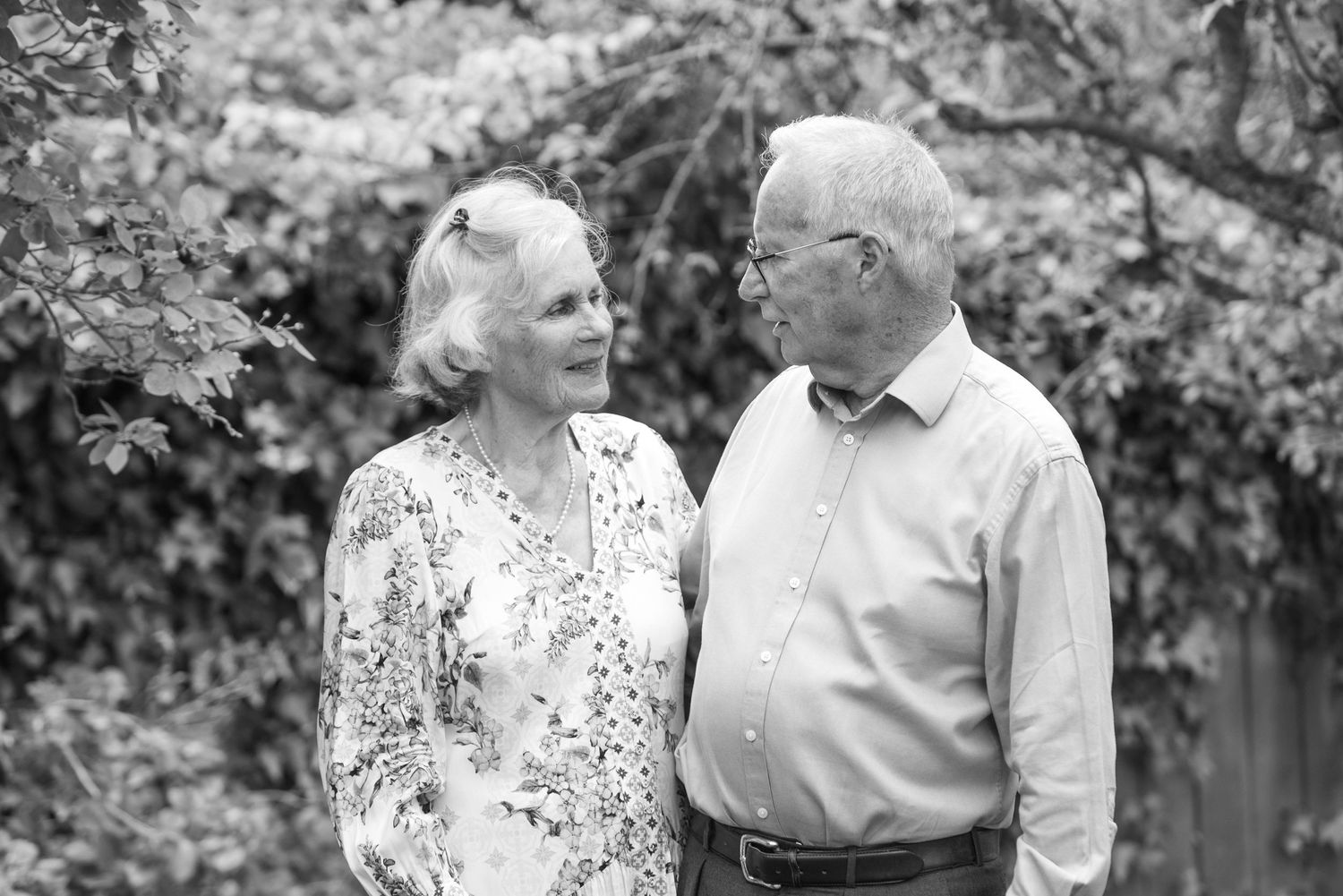 Elderly couple smiling at each other in a garden, black and white portrait photo.