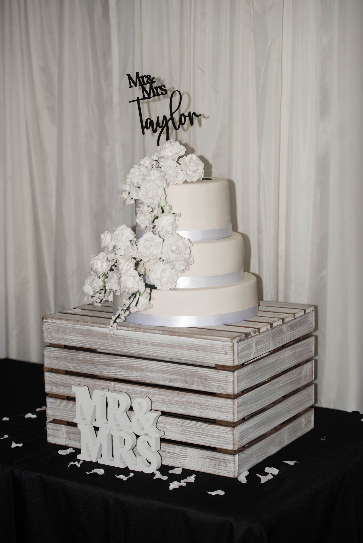 Four-tier white wedding cake with floral cascade on rustic wooden crate stand reading Mr & Mrs.