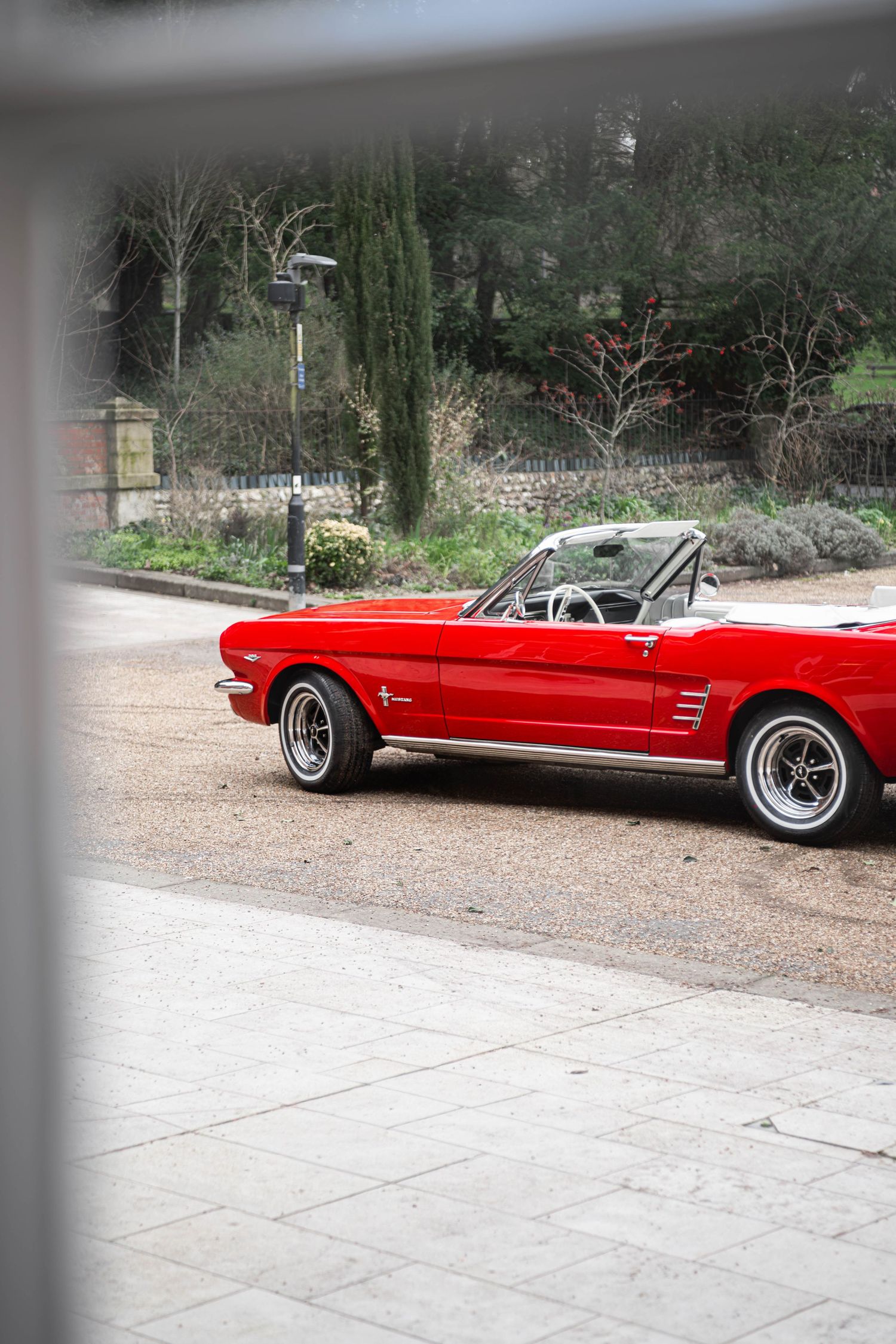 Classic red Ford Mustang convertible parked outside near a lush garden on a wedding day.