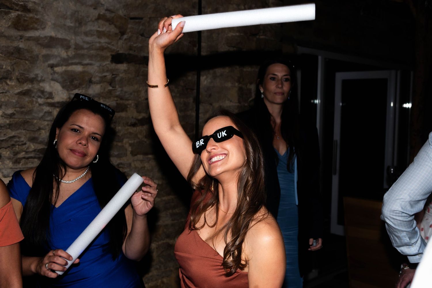 A woman wearing sunglasses dances energetically holding a glow stick at a lively wedding reception.