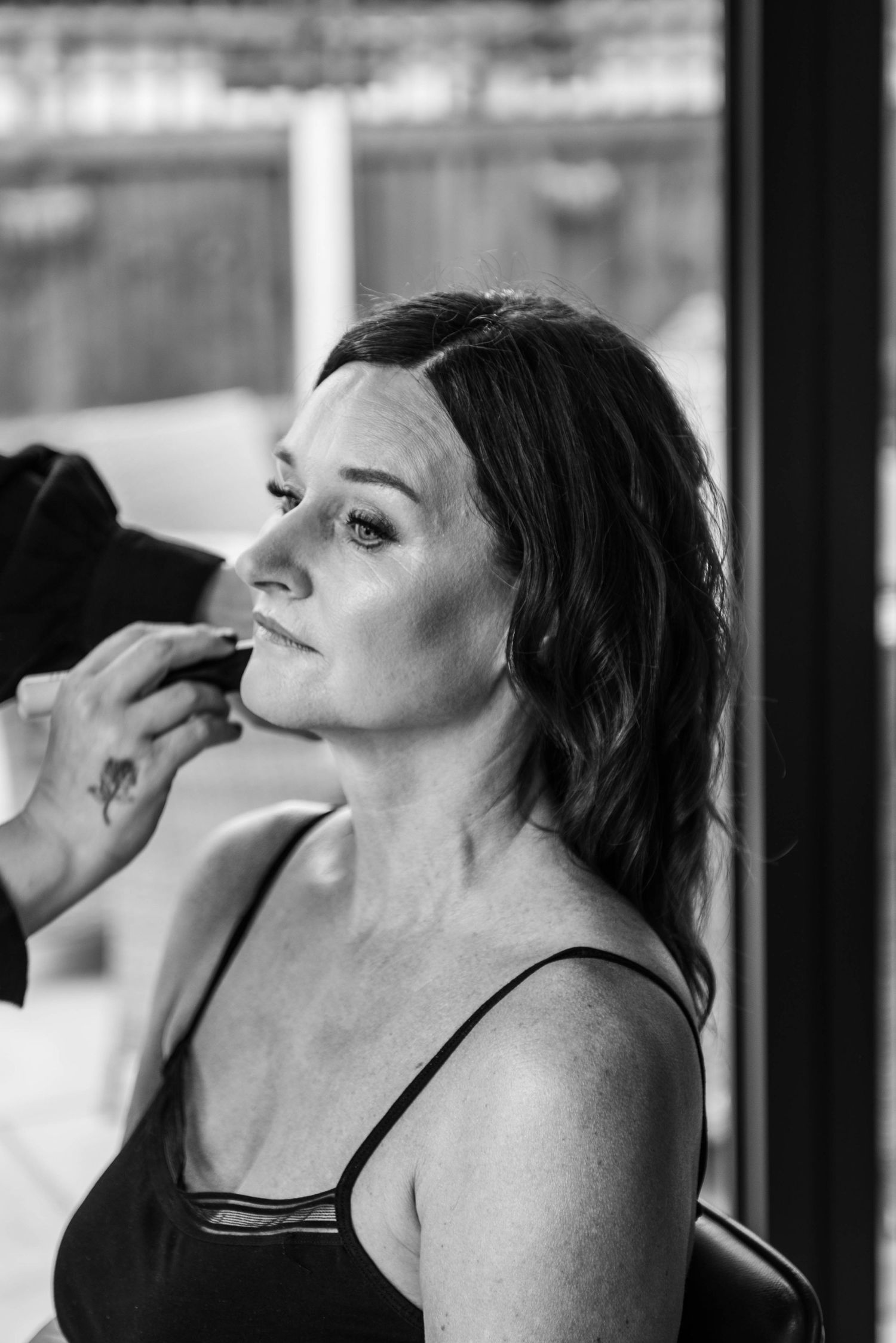 Black and white close-up of woman having makeup professionally applied during bridal preparation.