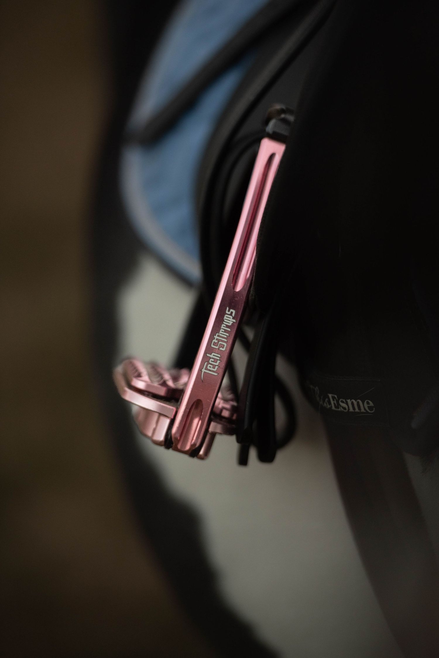 Pink metallic stirrup iron with engraved branding attached to a black leather saddle flap.
