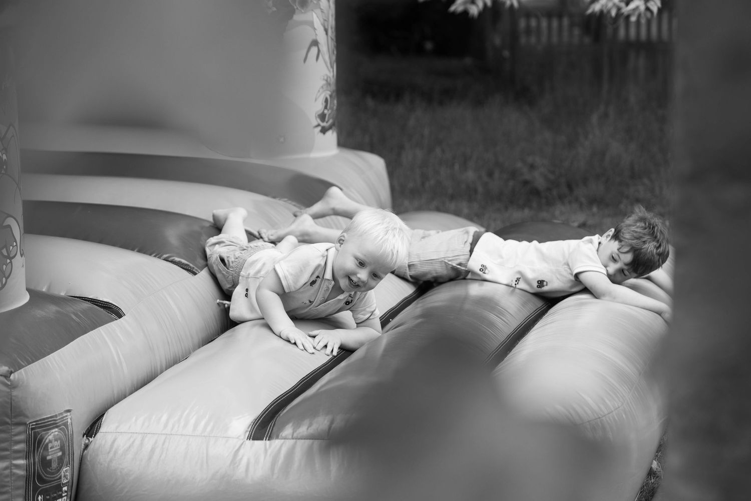Two young children resting on an inflatable bouncy castle in black and white photo.