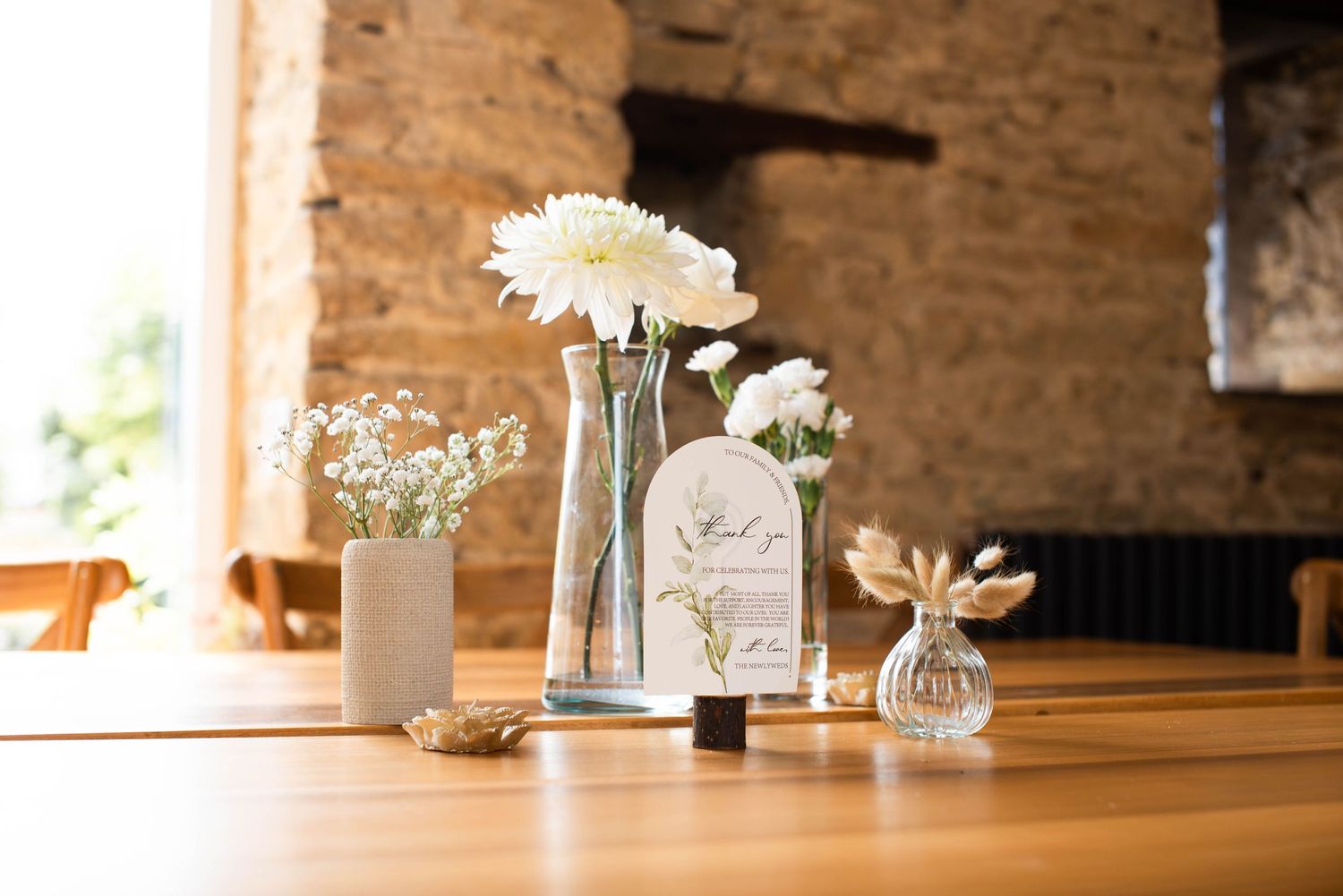 Elegant wedding table centerpiece with white flowers in glass vases and decorative card.