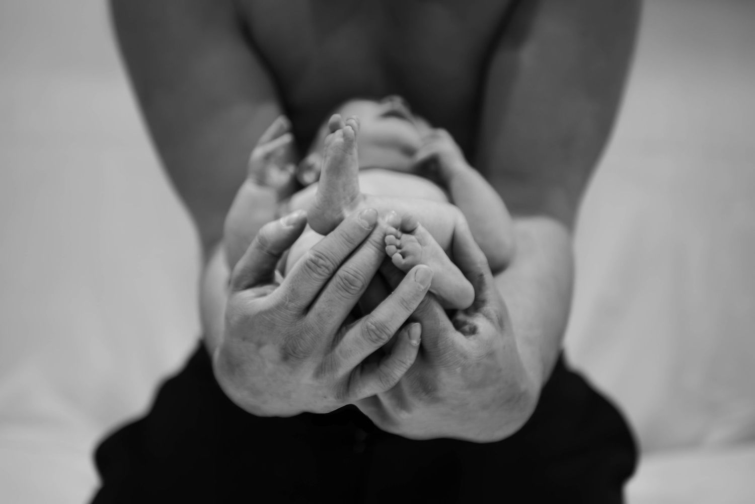 Black and white close-up of a parent tenderly cradling a newborns tiny feet in their hands.