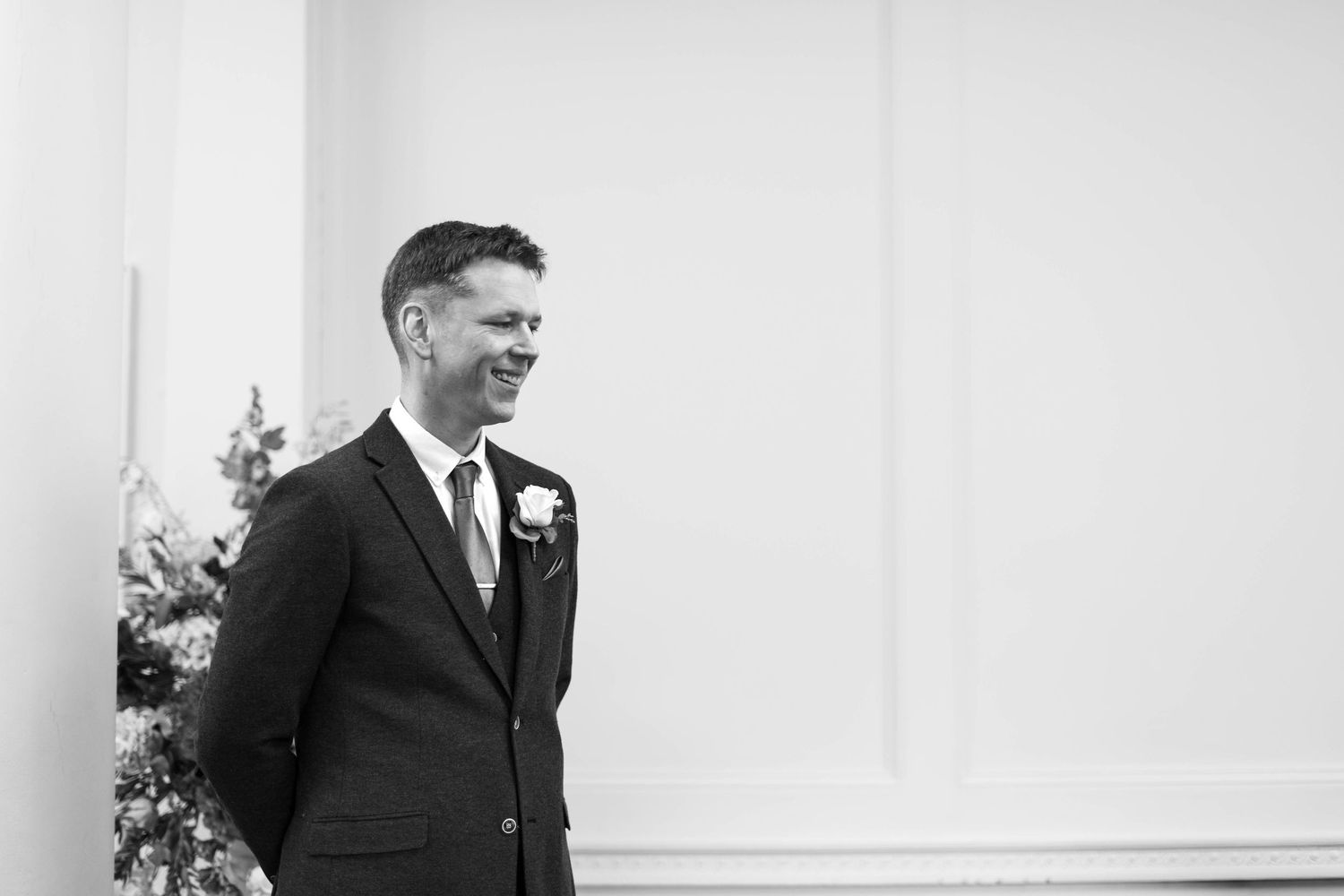 Dapper groom smiling in a dark suit with boutonniere during wedding ceremony in black and white.