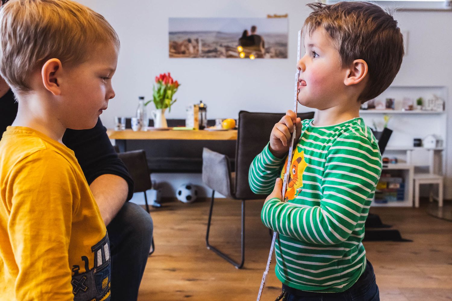 Familienreportage: Geschwisterfoto von Zwillingen die sich mit dem Metermaß abmessen um ihre Größe zu vergleichen.