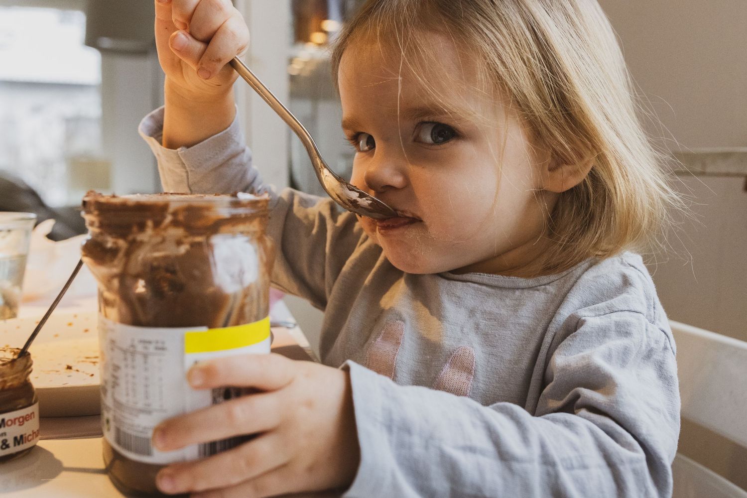 Fotoshooting beim Sonntagsfrühstück zu Hause bei der Familie: Auf dem Bild ist ein kleines Kind zu sehen das aus dem Nutella Glas löffelt.
