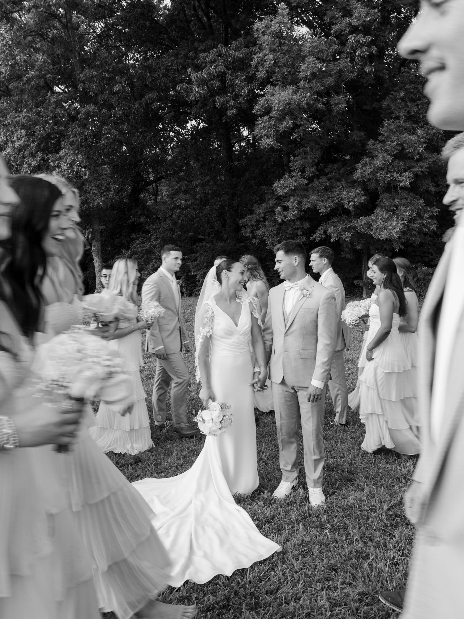 Black and white wedding photo of bride and groom sharing a moment surrounded by bridal party outdoors in Tennessee.