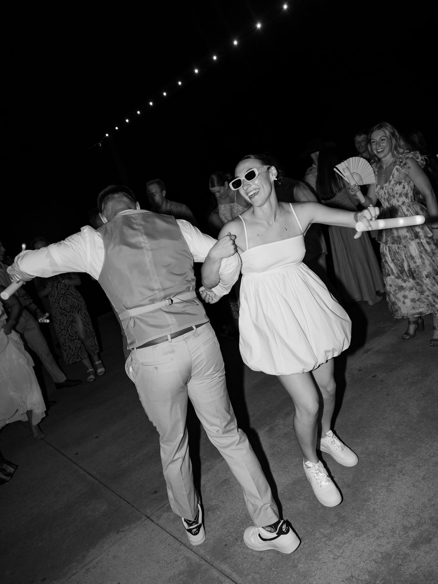 Bride and groom dancing joyfully at nighttime outdoor wedding reception wearing sunglasses and sneakers in Tennessee.