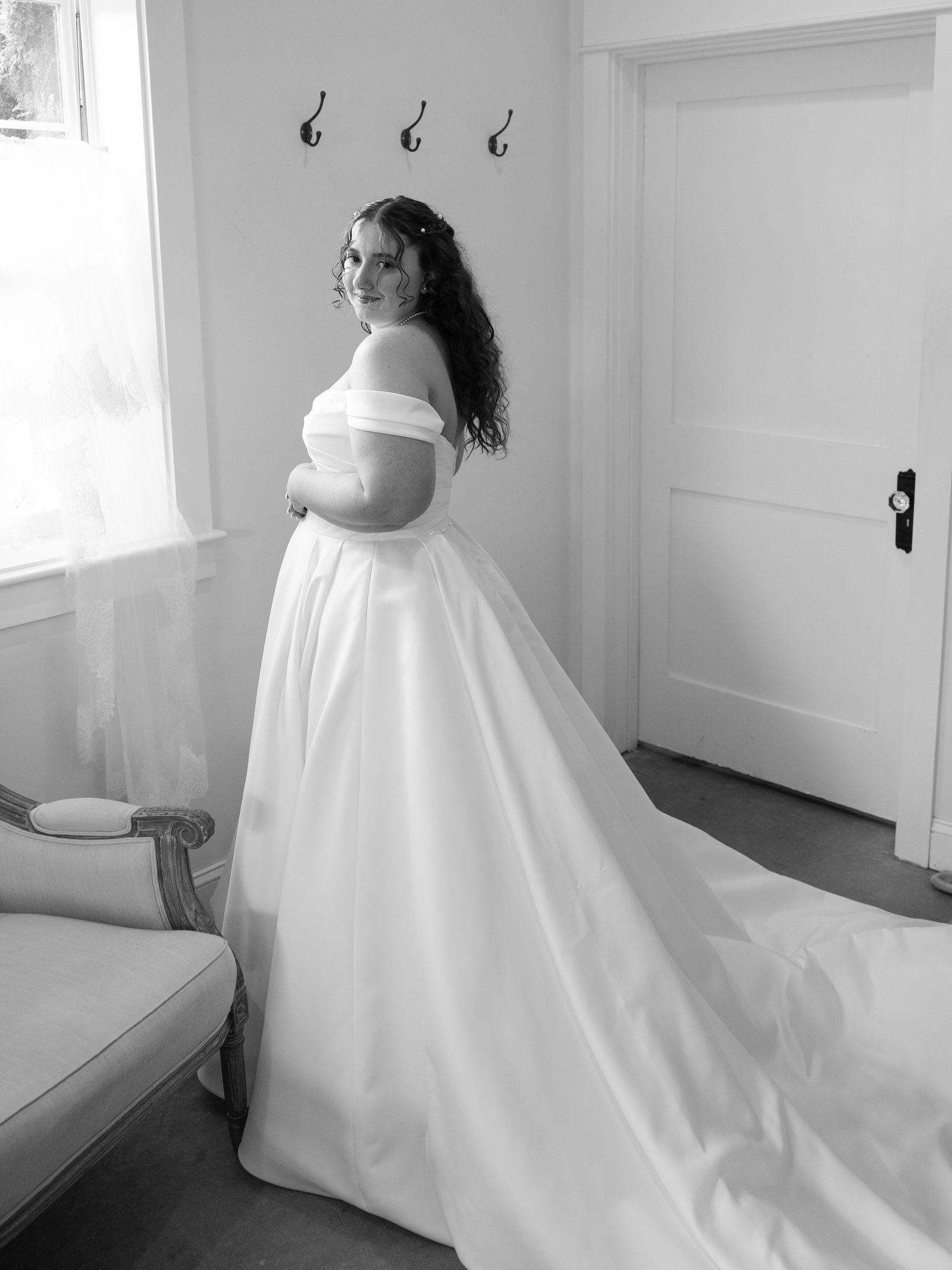 Bride in off-shoulder ball gown wedding dress with long train poses in black and white photo.