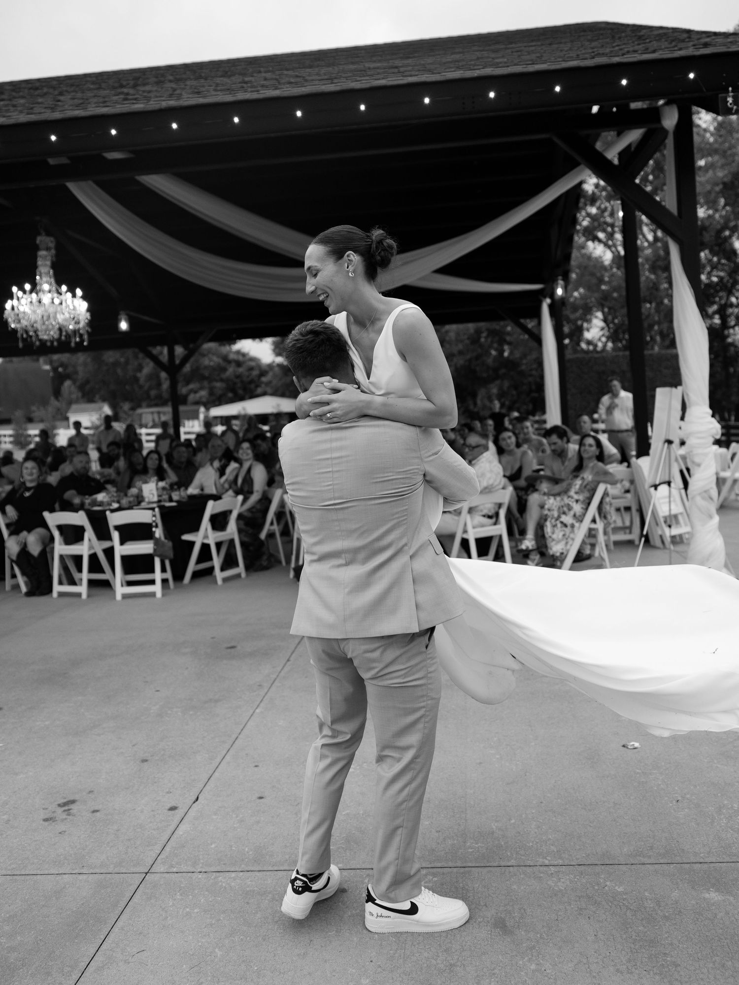 Groom lifting bride during first dance at outdoor wedding reception under draped pavilion with chandelier in Tennessee.