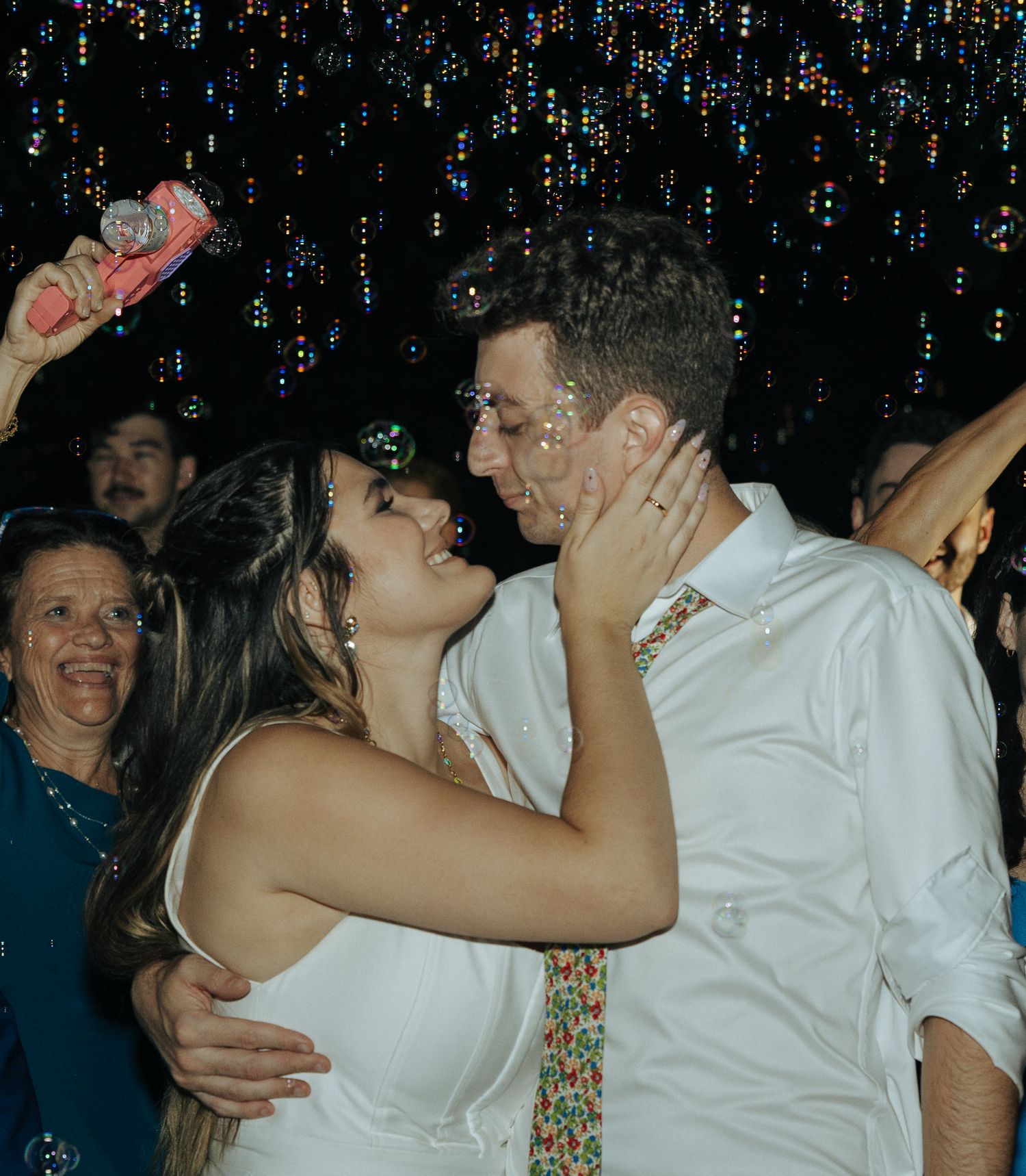 Newlyweds share a romantic kiss on the dance floor under glittering lights during their wedding reception celebration.