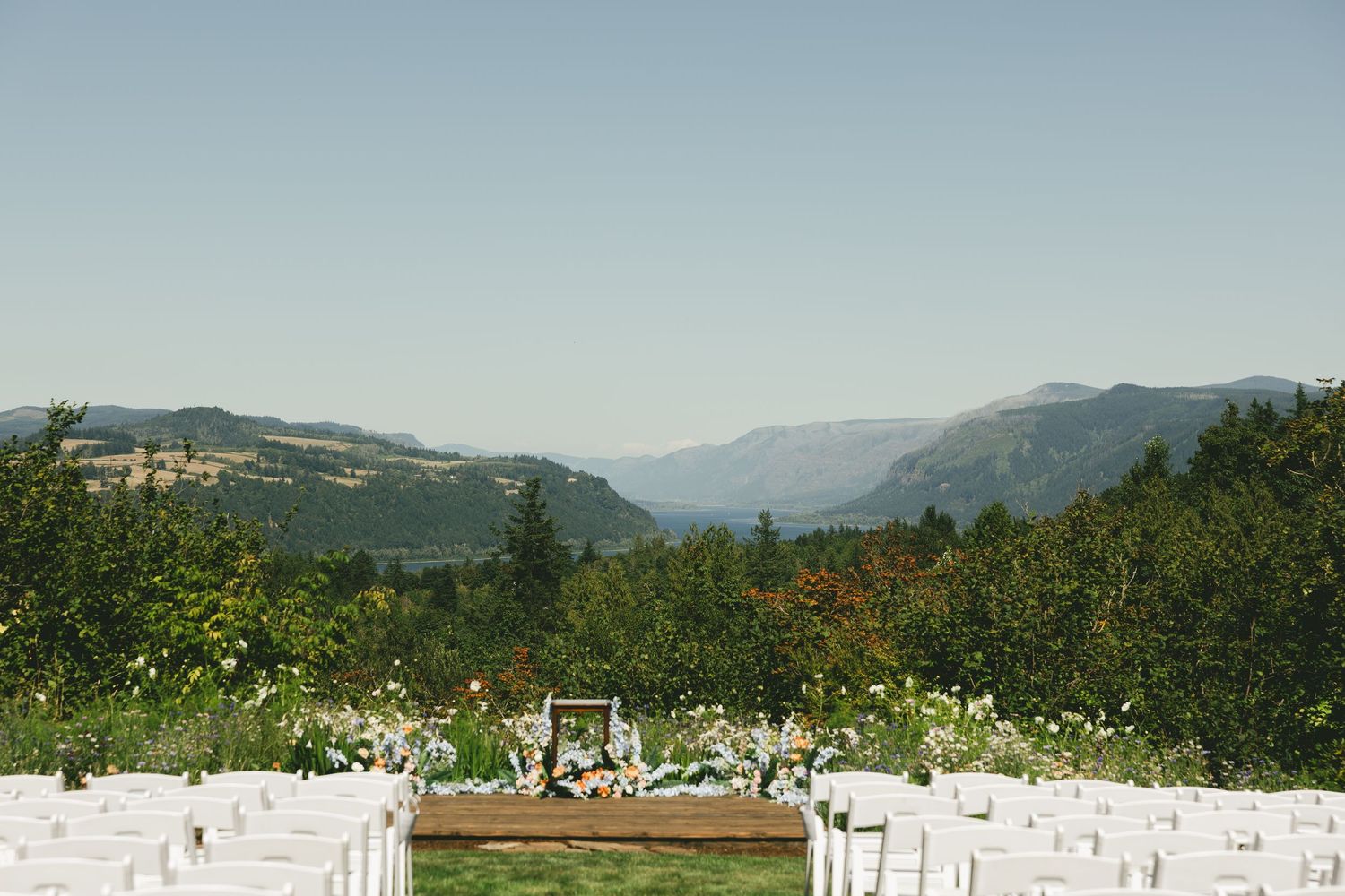 White ceremony chairs set up outdoors with mountain views and lush greenery creating a scenic wedding backdrop.