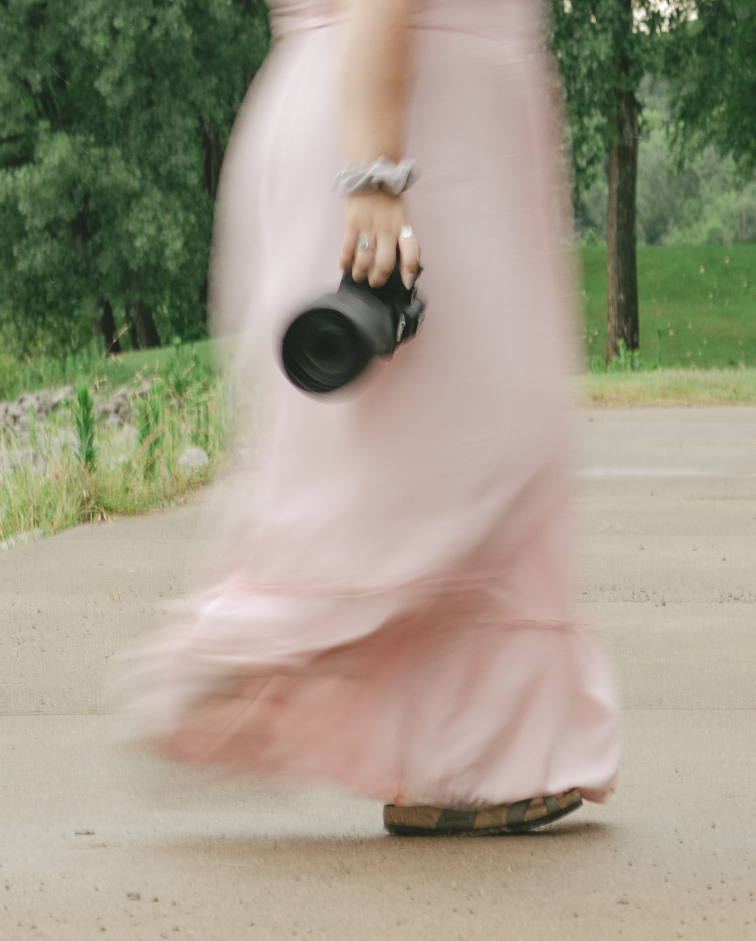 A figure in a flowing pink dress walks on a path holding a black mug, creating a dreamy motion-blur effect.