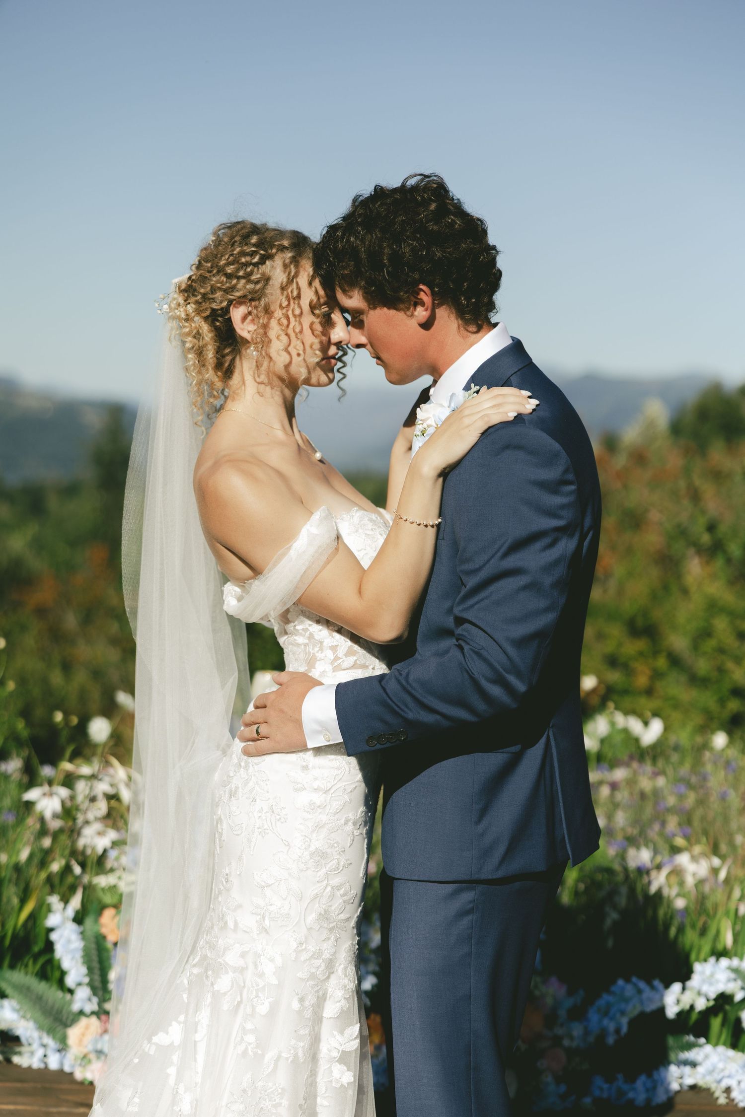A romantic outdoor wedding moment with newlyweds embracing in a scenic garden setting filled with flowers.