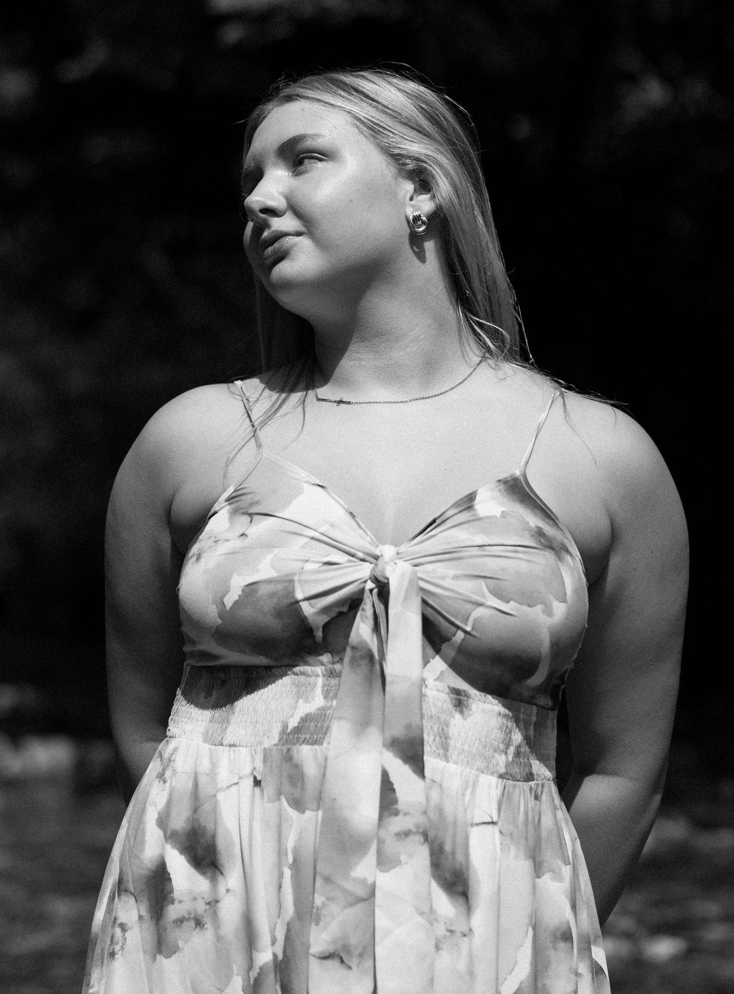 A black and white portrait of someone wearing a floral sundress with a tied bow detail at the neckline against a dark background.