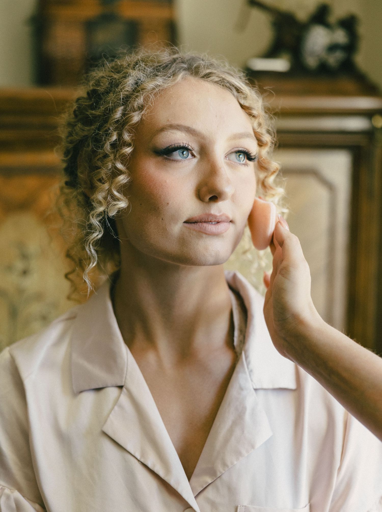 Portrait shot of a woman with curly blonde hair and blue eyes wearing a cream colored collared shirt.