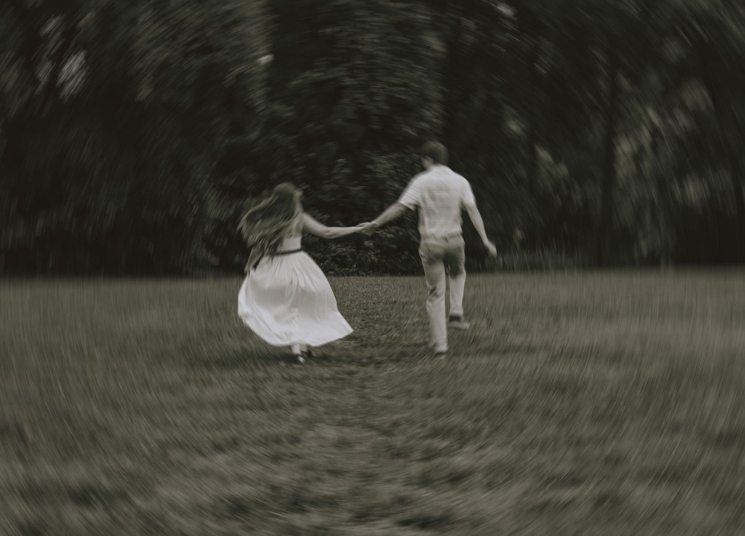 A couple dances together in a dreamy, black and white scene on a grassy field.