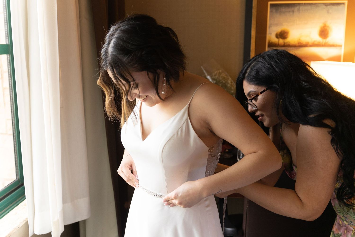 A bride getting ready for her wedding day while a bridesmaid helps her with her dress