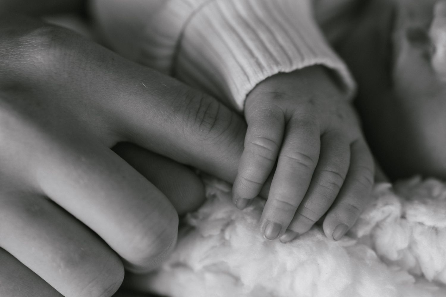 Close-up of gentle baby hands holding mother's finger on soft fabric in black and white.