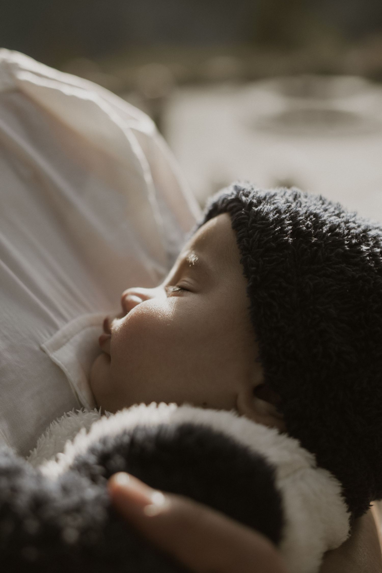 A sleeping infant nestled in soft white bedding with natural lighting creating a peaceful atmosphere.