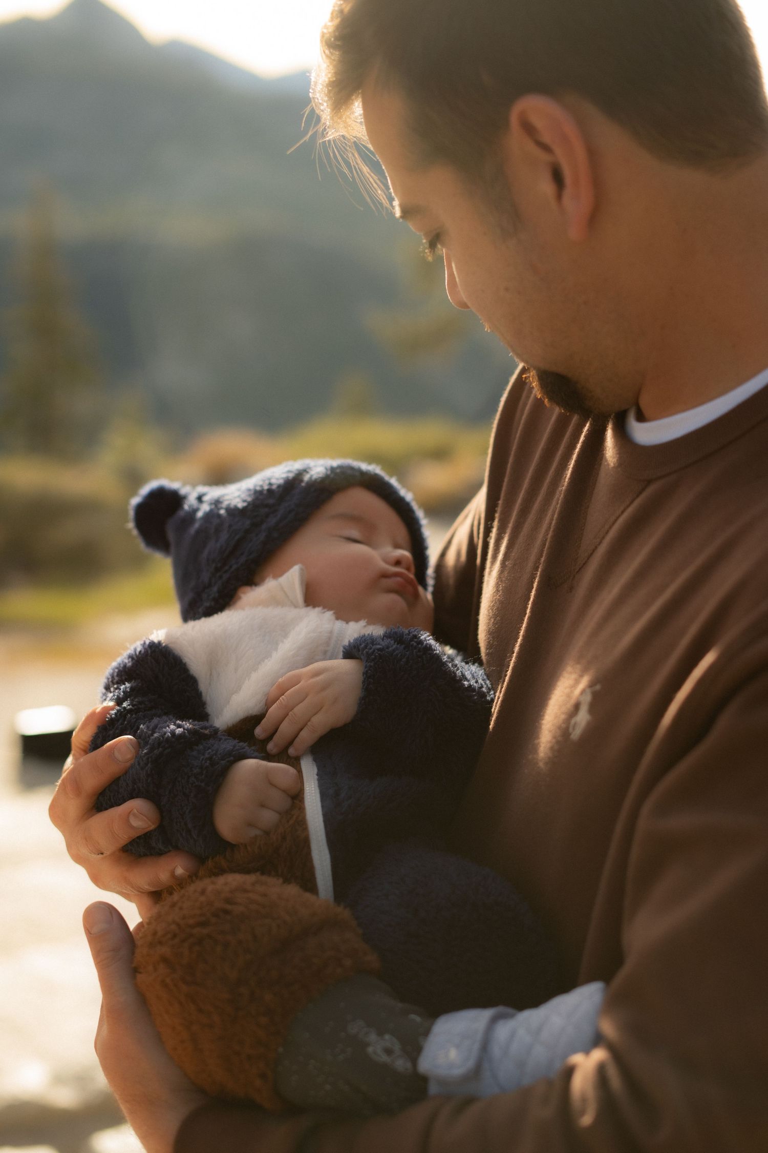 A tender moment captured outdoors as a baby in winter clothing rests against a brown sweater.