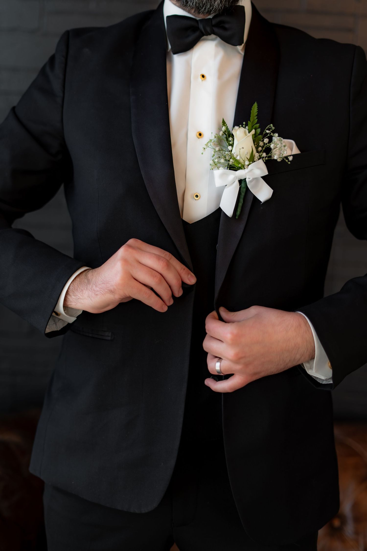 Close-up detail of black tuxedo with white boutonniere and bow tie.