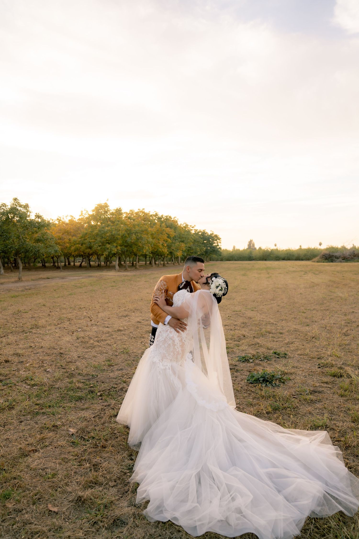 Bride in flowing white gown laying gracefully in an open field at sunset.