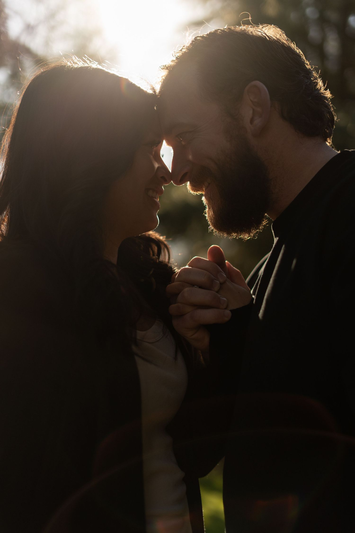 Silhouetted couple holding hands and gazing at each other in golden sunlight.
