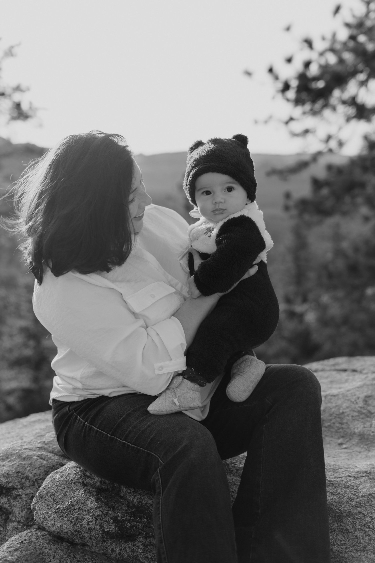 Black and white portrait of parent and baby sitting on rocky overlook.