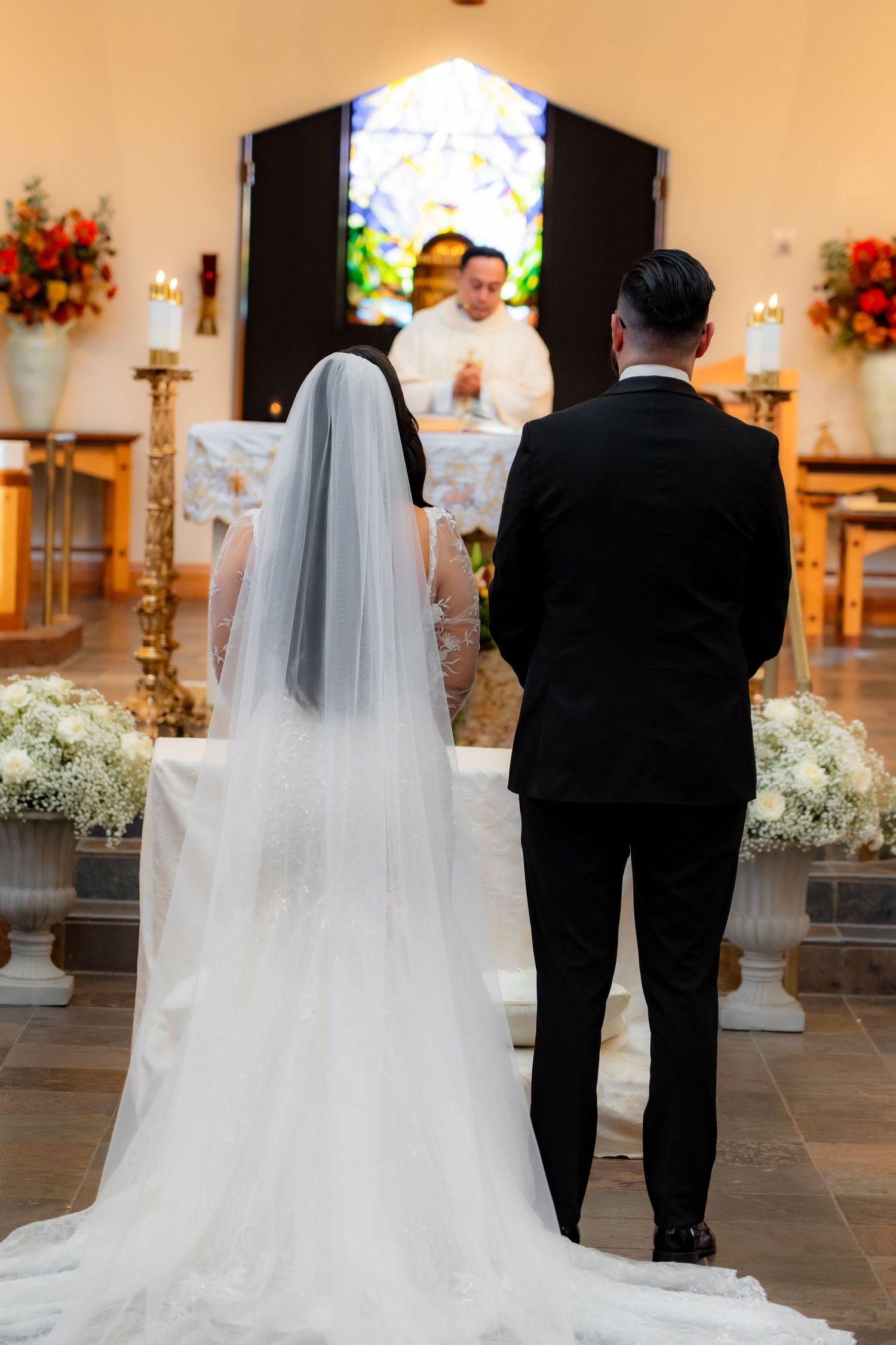 Bride and groom standing at church altar with flowing white veil and traditional decorations.