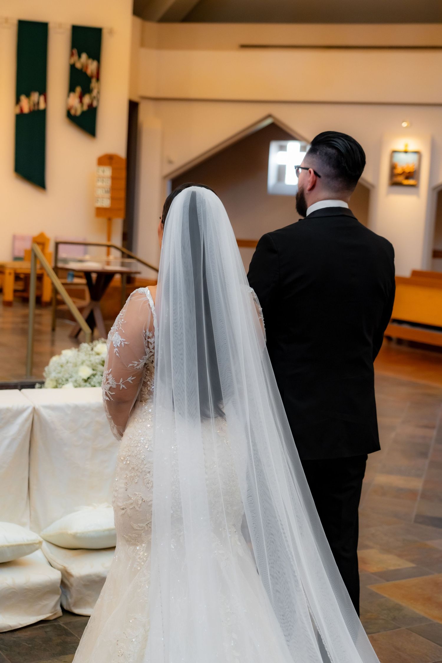 Wedding couple standing together in church with bride wearing long flowing veil.