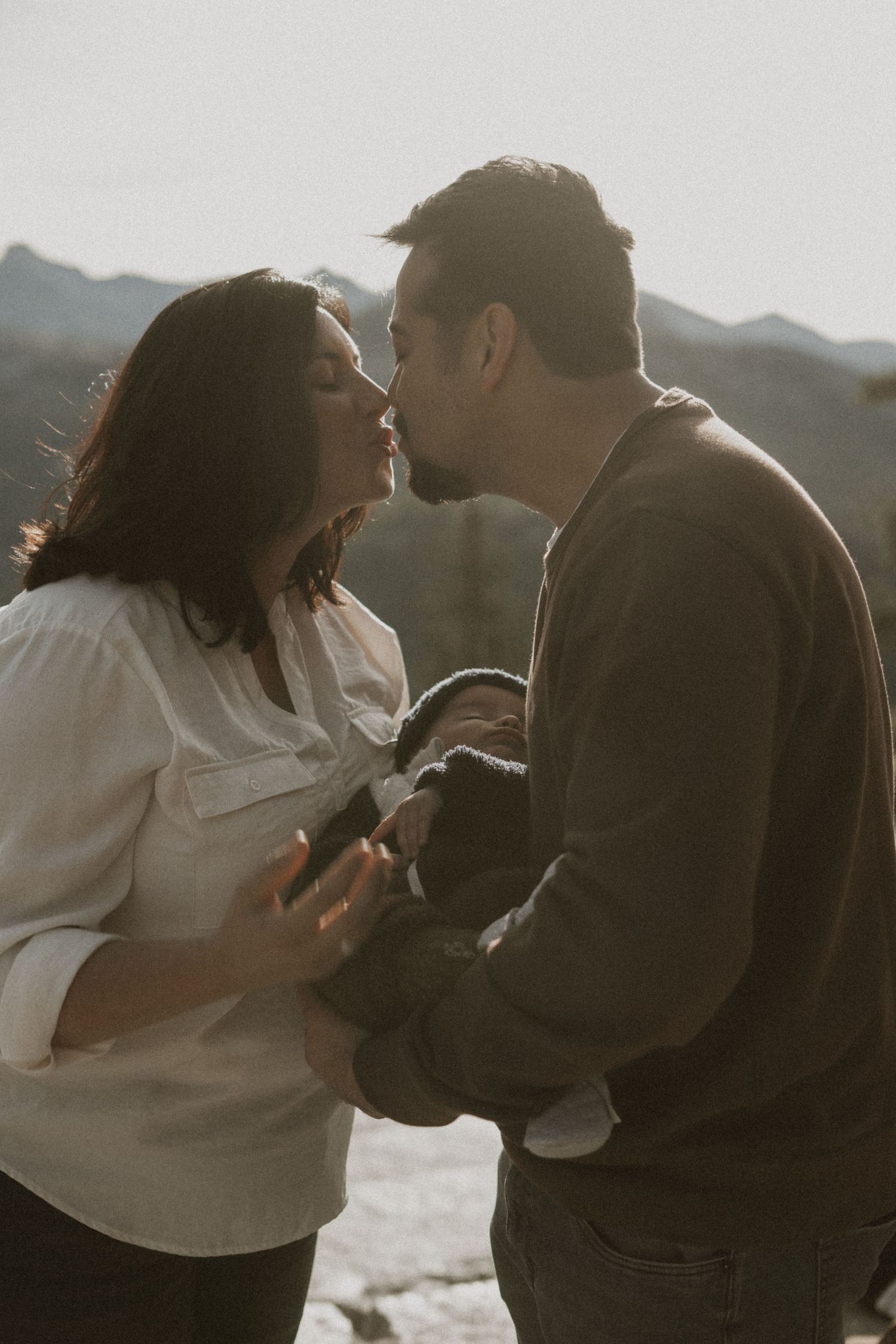 Intimate family portrait with mountain backdrop as couple shares tender moment with baby.