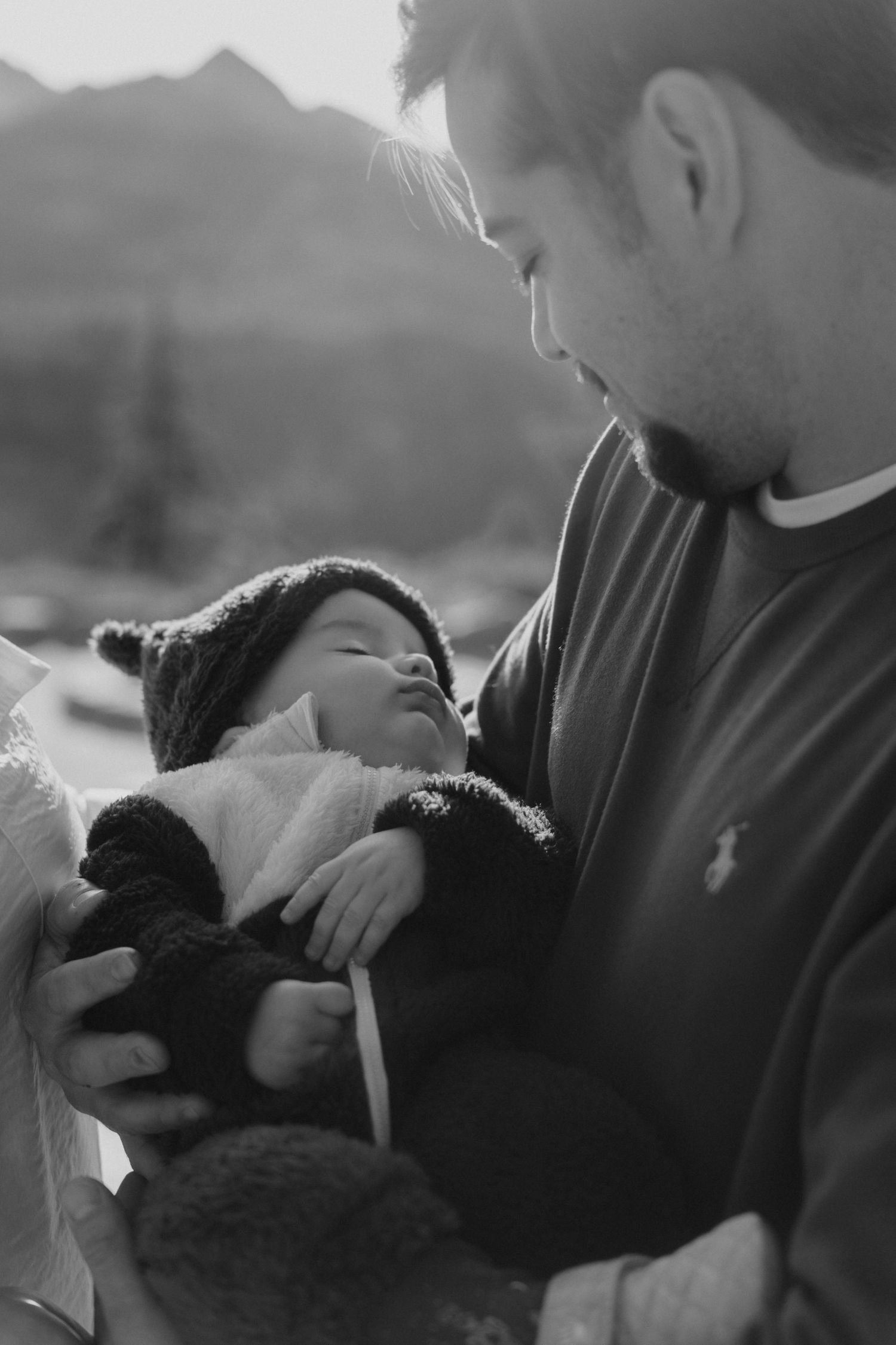 Black and white portrait of a nurturing moment against a mountainous backdrop.