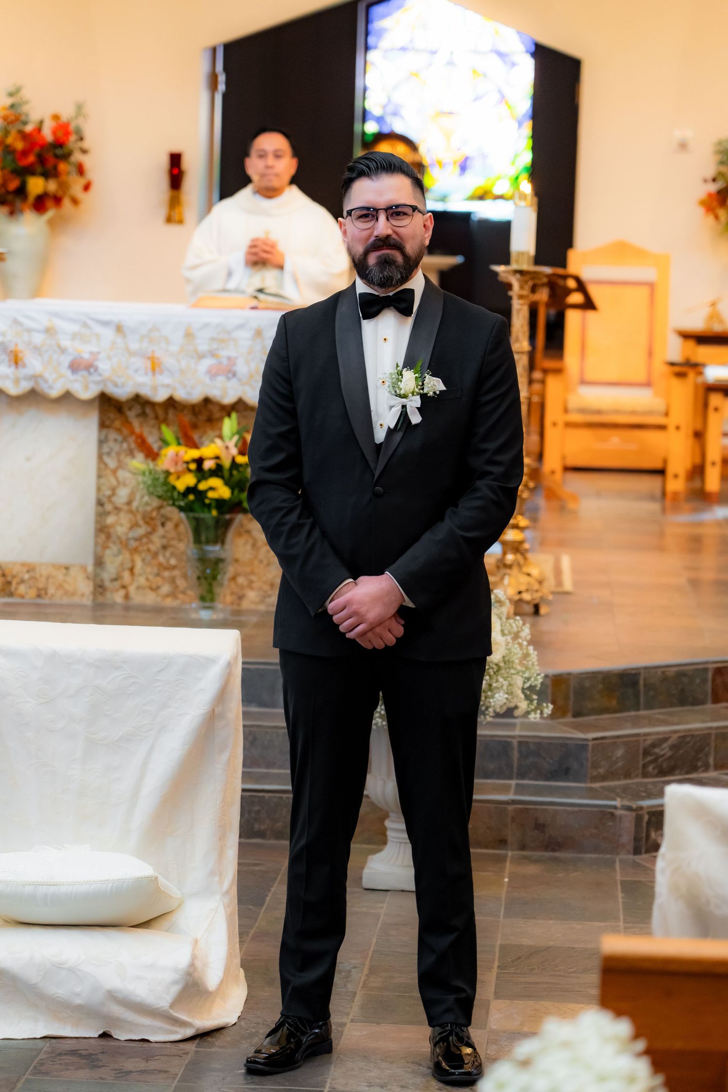 Groom standing at altar wearing classic black tuxedo during wedding ceremony.