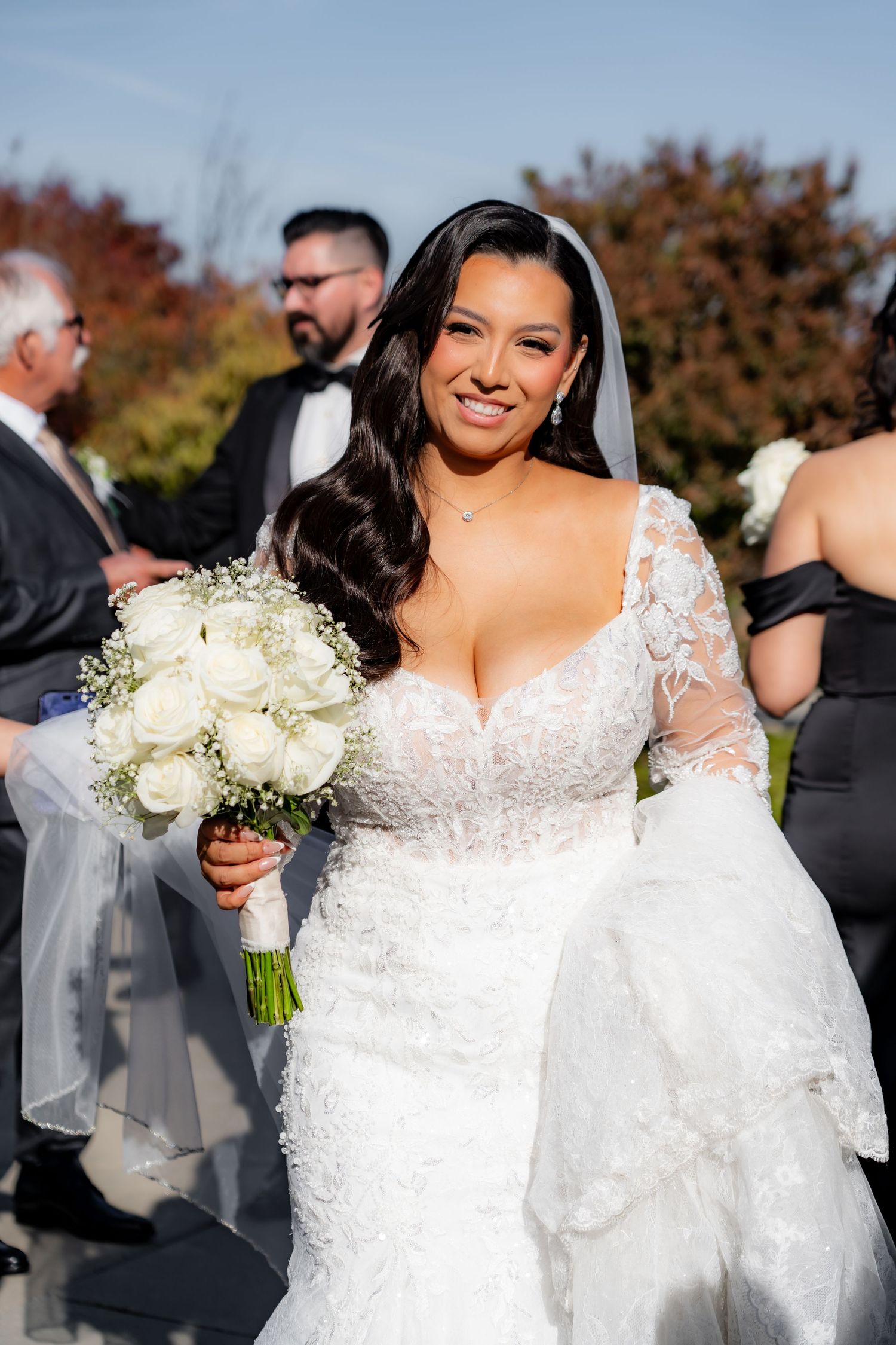Bride in a white lace gown holding a bouquet of white roses during outdoor wedding photos.