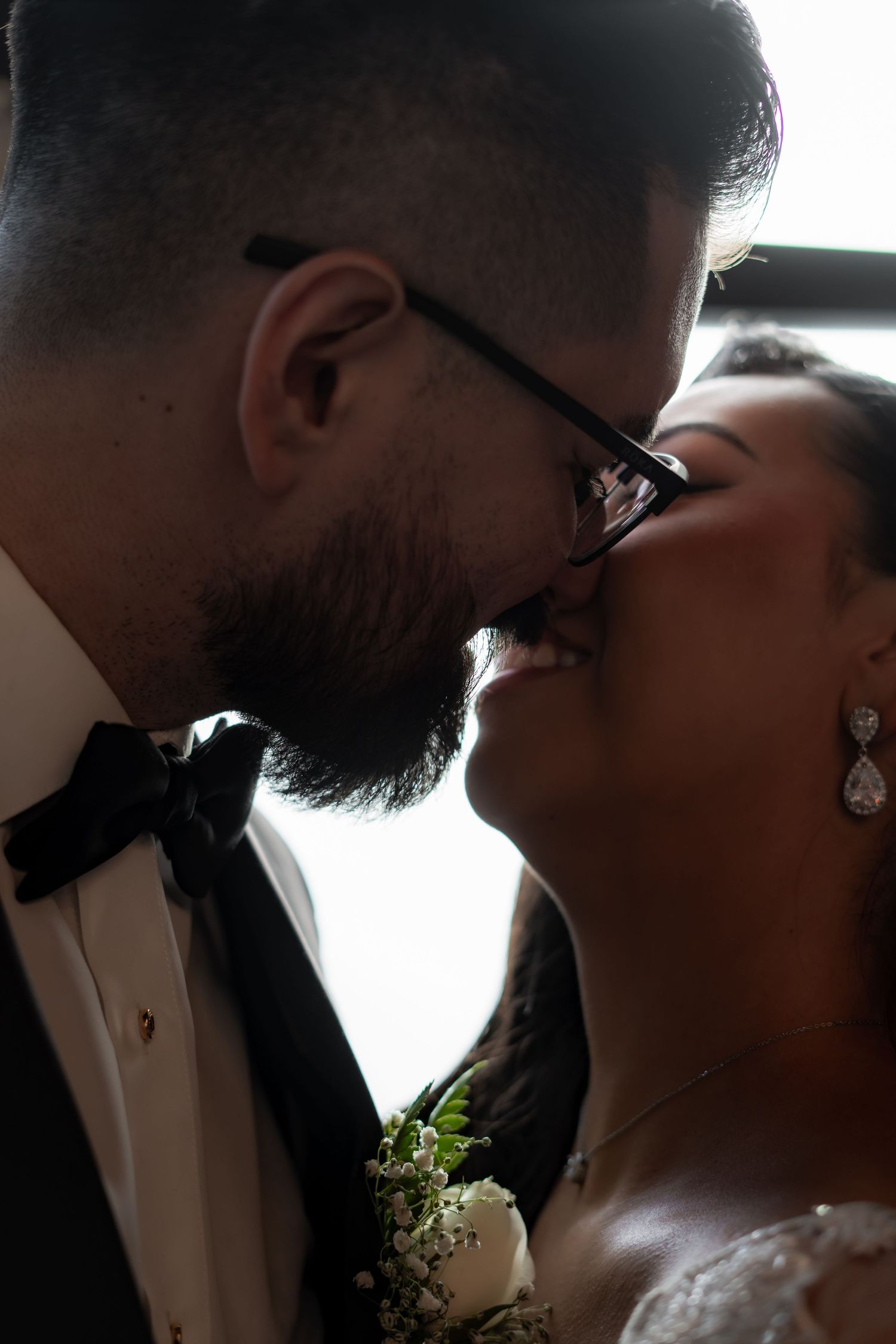 Close-up silhouette profile of newlyweds sharing a tender moment in front of a window.
