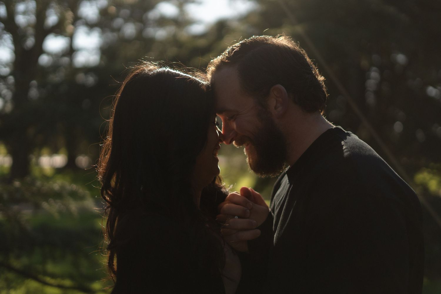 Couple sharing an intimate moment with sunlight filtering through trees.