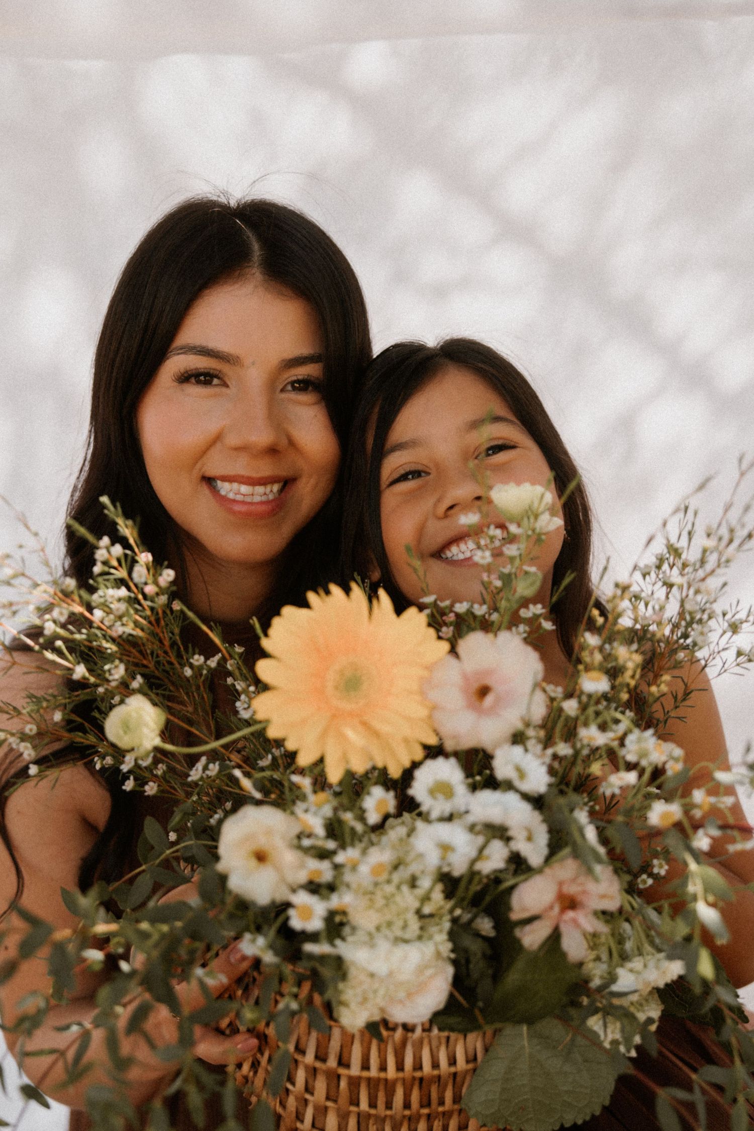 A smiling woman and young girl hold a beautiful bouquet of wildflowers including gerbera daisies and baby's breath.