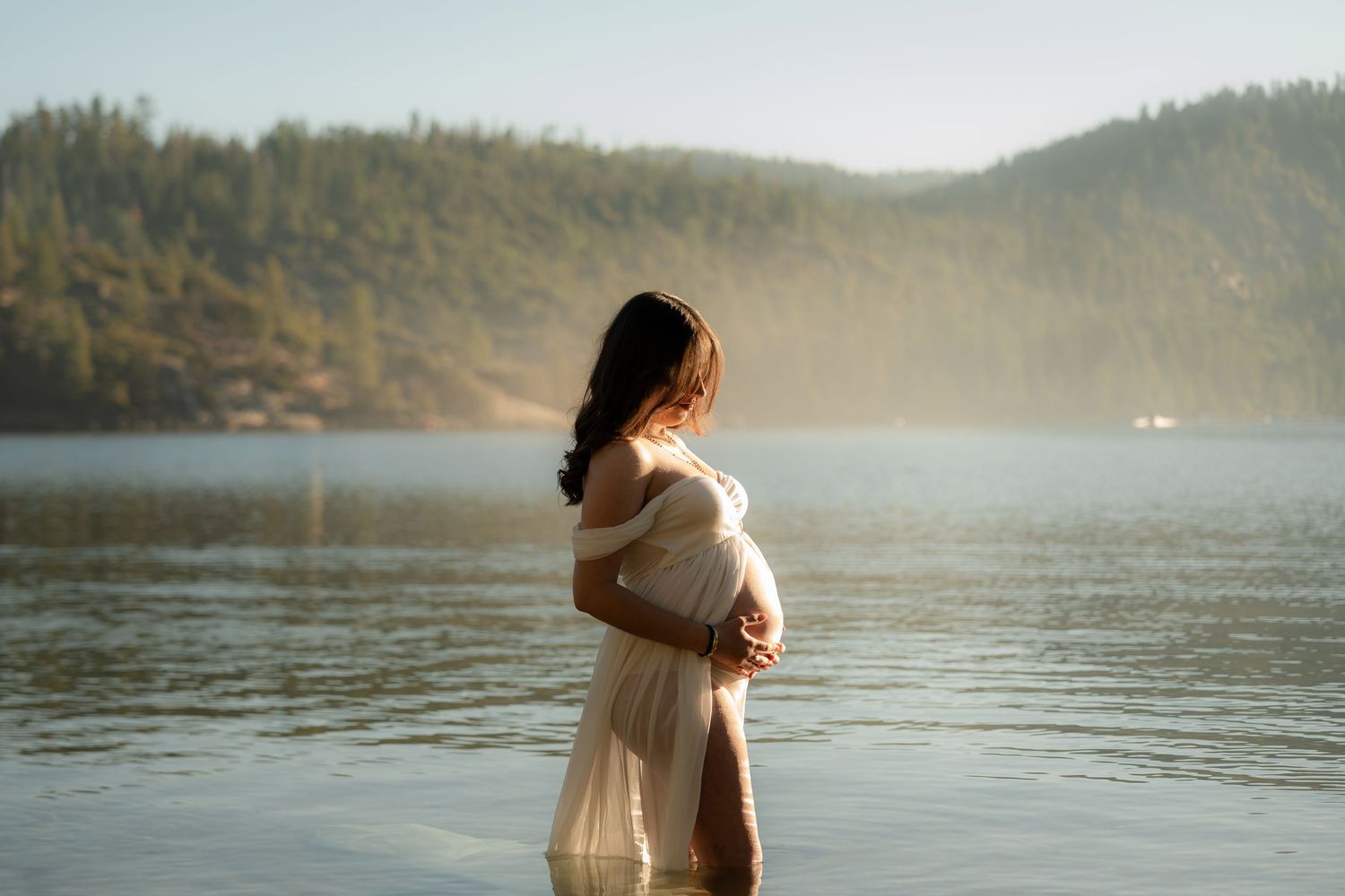 A couple embraces by a misty lake surrounded by mountains during a romantic photoshoot at sunset.