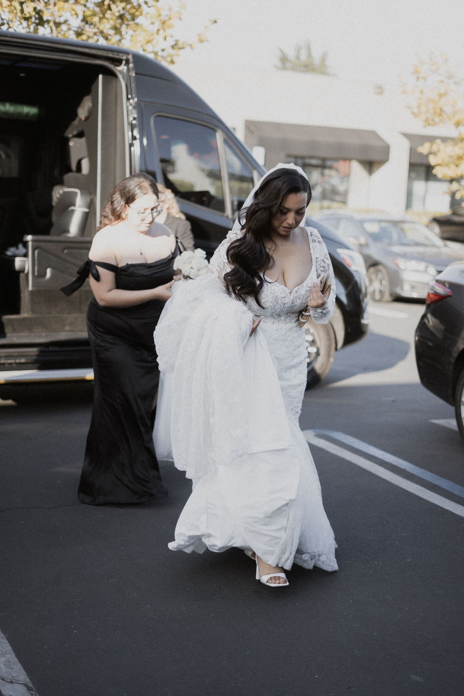 Wedding day arrival with elegant white gown flowing in the breeze beside a black van.