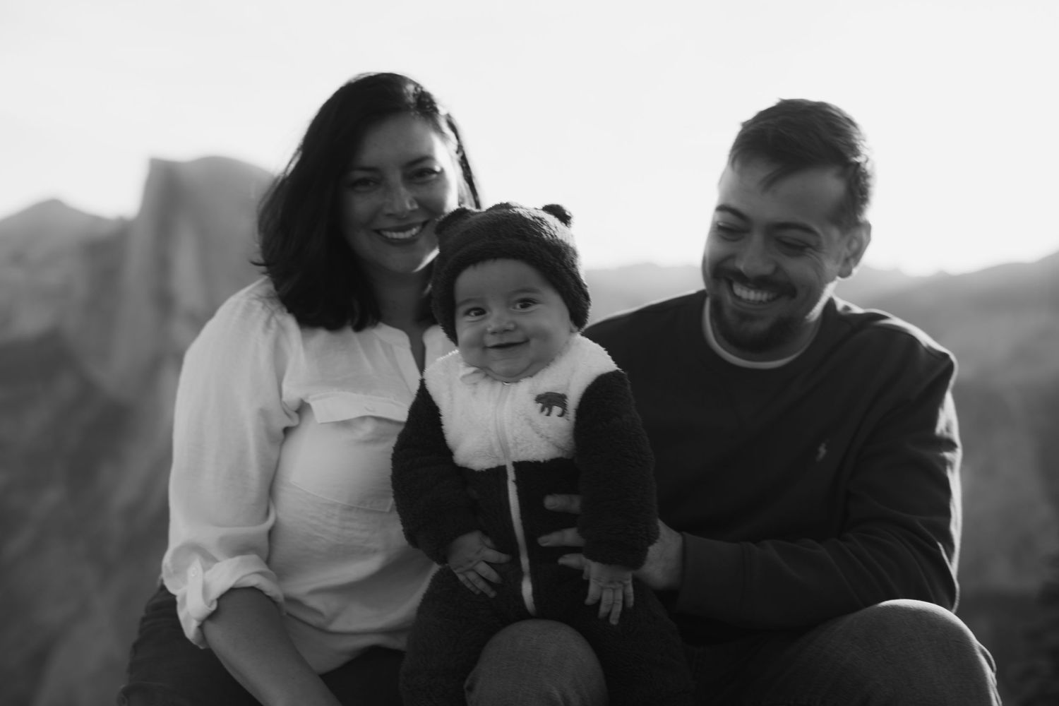 Family sitting together outdoors on a mountain overlook during a casual photoshoot.