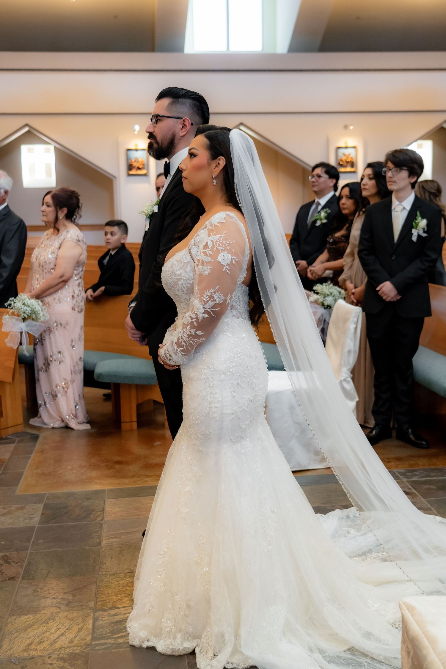 Couple in formal wedding attire kneeling during traditional church ceremony.