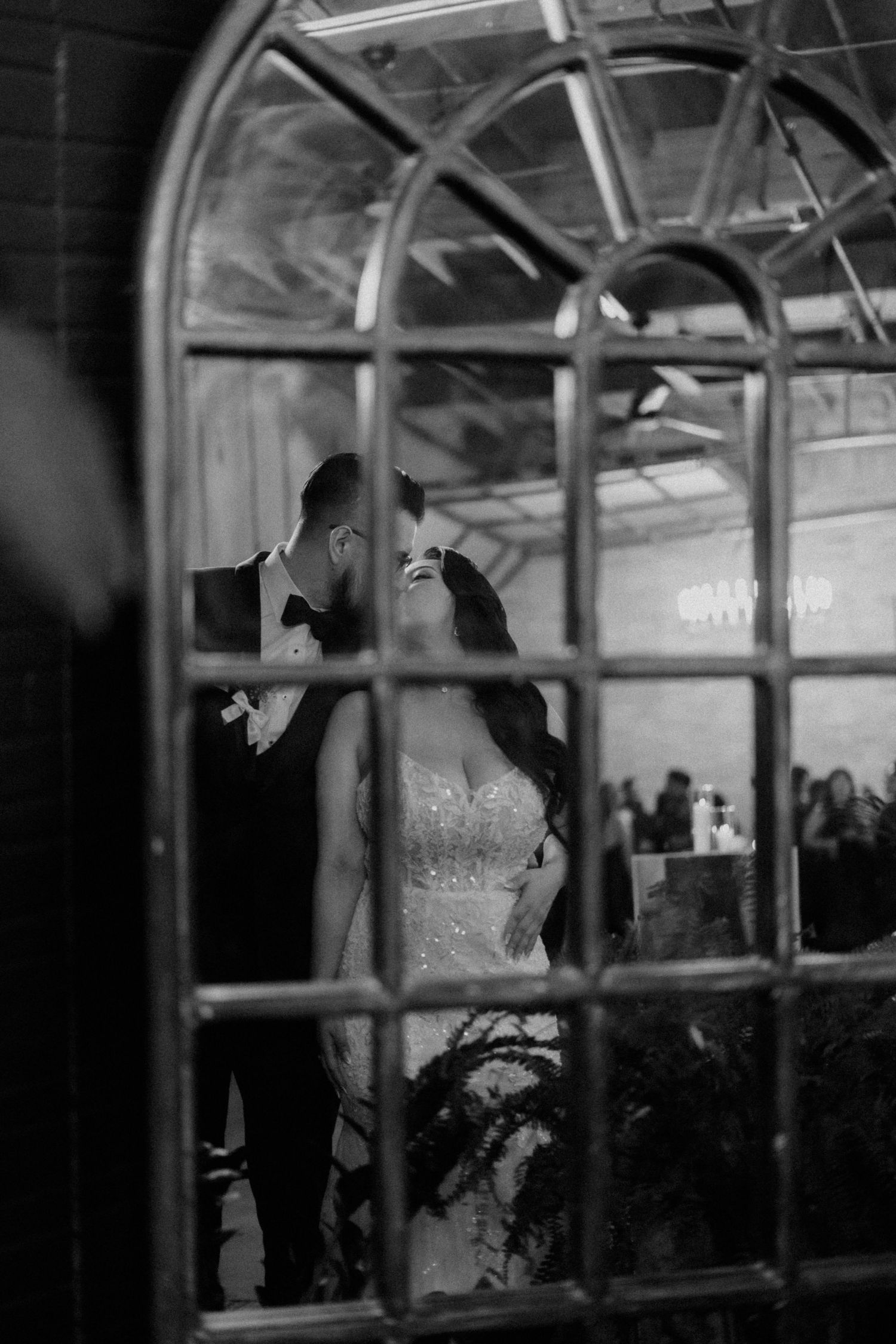 Silhouettes of a wedding couple seen through an arched window frame.