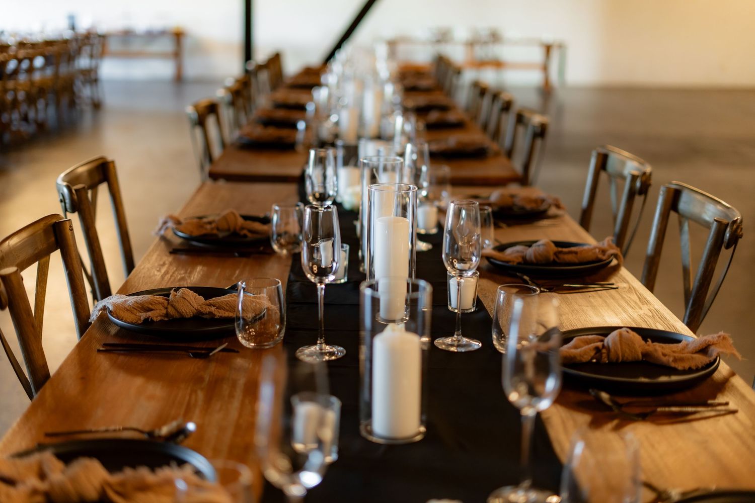 Long wooden dining table elegantly set with black placemats, wine glasses and table settings for a formal event.