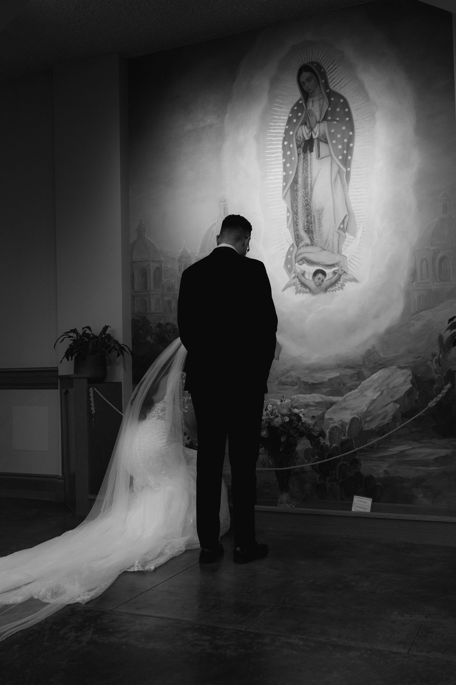 Dramatic black and white photo of couple in front of religious mural during wedding ceremony.