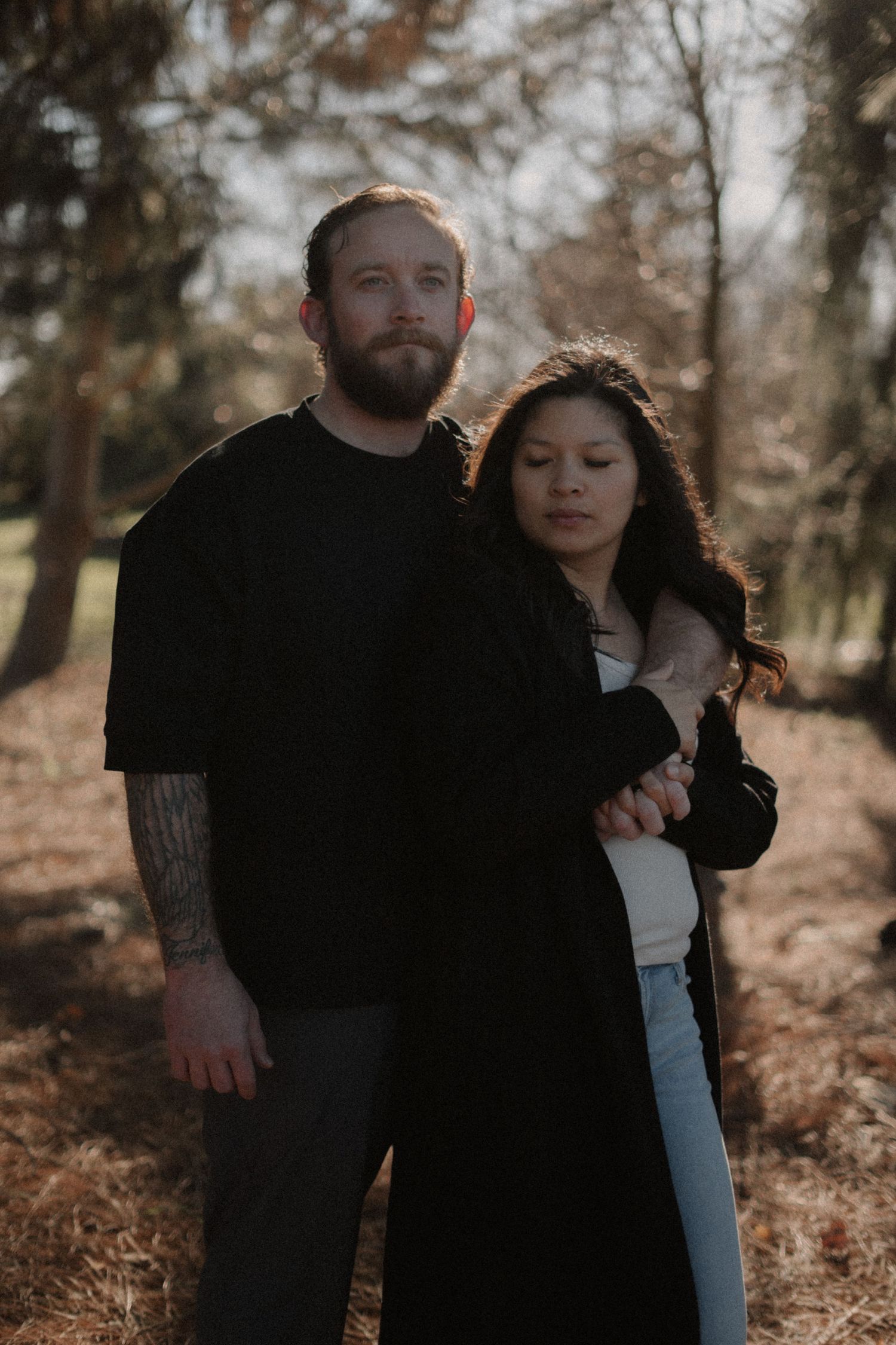 A romantic couple embraces in a wooded outdoor setting during golden hour.